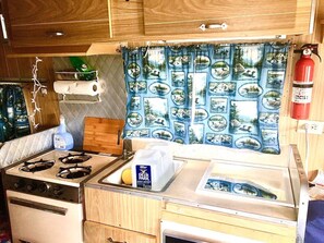 A compact kitchenette with a stove, sink, and a small countertop. - 1966 Shasta Cottage w/AC - Durham, NC (Durham)