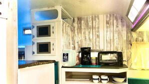 Uma kitchenette compacta com micro-ondas, cafeteira e um pequeno armário com chávenas e tigelas.