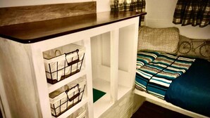 Um quarto pequeno com uma cama, um armário branco com caixas organizadoras e uma prateleira de madeira.