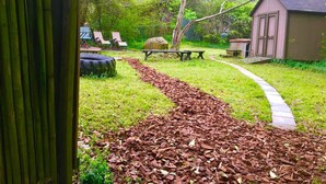Um jardim com um caminho sinuoso, mesas para piquenique e um galpão.
