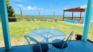 Un patio cubierto con una mesa y sillas de vidrio, con vistas a una piscina y un paisaje pintoresco.