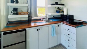 Una cocina moderna con armarios blancos, encimera de madera, barra de café y ventana con cortinas.
