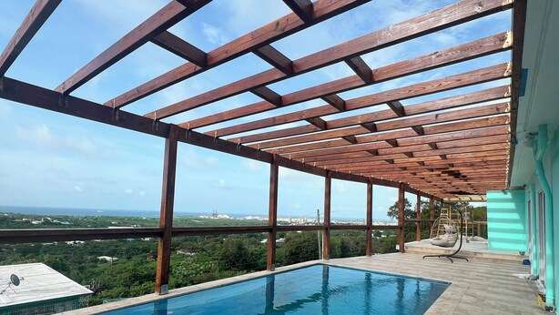 Una piscina en la azotea con una pérgola de madera, vista al océano y un deck de baldosas.