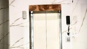 An elevator with a marble wall design, a metallic door, and a wall-mounted phone. - Hotel Holy City (Amritsar)