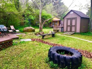 Ein Garten mit einem Reifenbeet, einer Holzterrasse mit Stühlen, einem kleinen Schuppen und einem Picknicktisch.