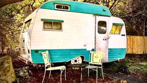 A vintage camper with a turquoise and white exterior, two chairs, and a small table in front. - Stay Like a Rock Star! - Tour Bus in Durham, NC (Durham)