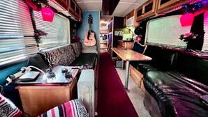 A narrow, well-lit RV interior with a red carpet, a guitar, a table, and a couch. - Stay Like a Rock Star! - Tour Bus in Durham, NC (Durham)