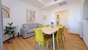 A modern living room with a dining table, yellow chairs, a grey sofa, and abstract wall art. - 4BNB - Baldo degli Ubaldi Big Apartment (Rome)
