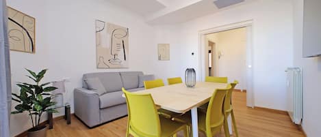 A modern living room with a dining table, yellow chairs, a grey sofa, and abstract wall art.