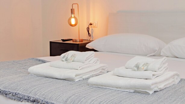 A neatly made bed with white pillows and folded towels, a bedside lamp, and a power outlet on a nightstand. - 4BNB - Baldo degli Ubaldi Big Apartment (Rome)