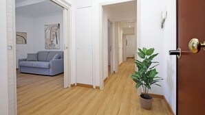 A hallway with a wooden floor, a grey sofa, and a potted plant. - 4BNB - Baldo degli Ubaldi Big Apartment (Rome)