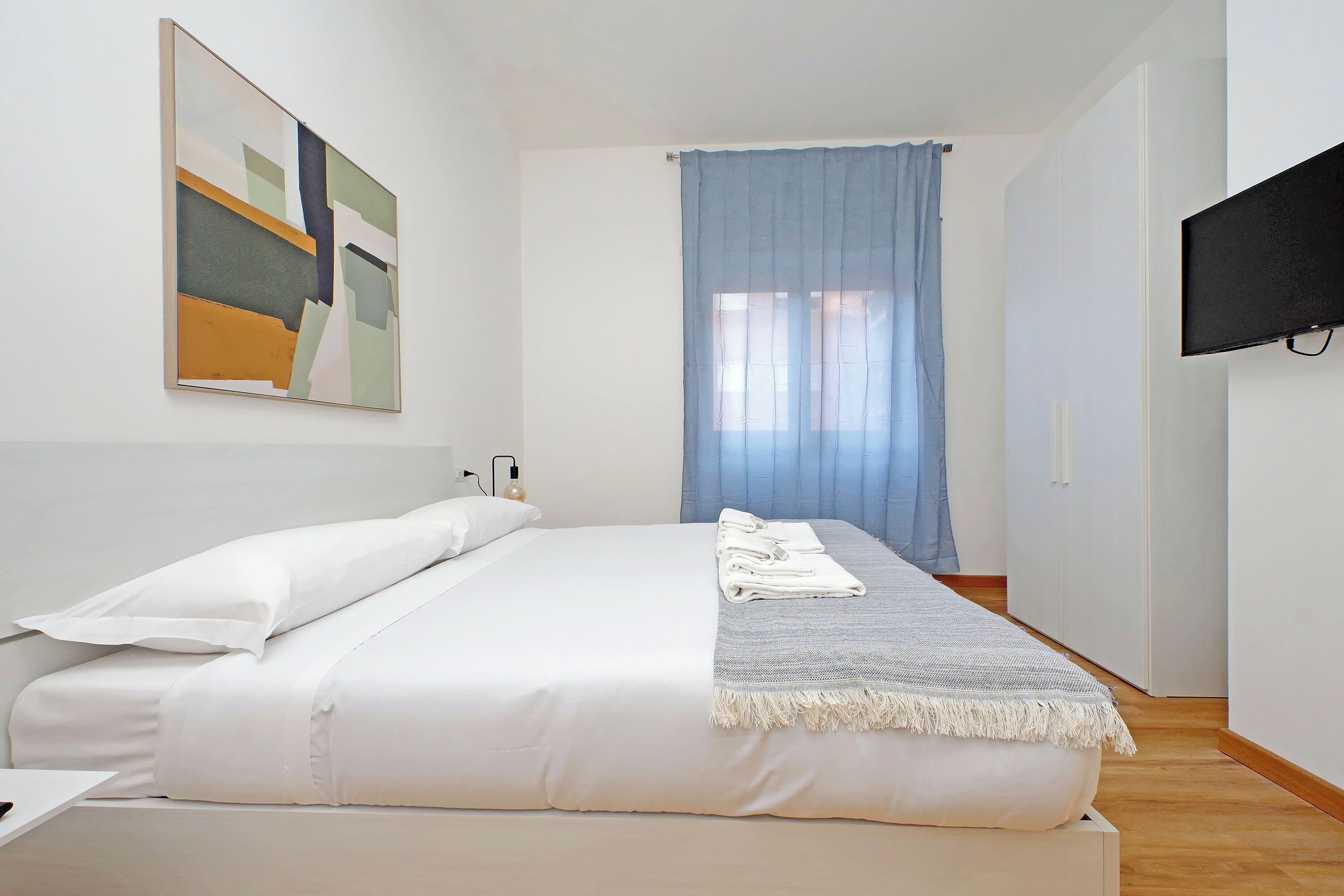 A bedroom with a bed, a TV mounted on the wall, and a window with curtains.