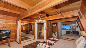 Acogedor dormitorio tipo cabaña de madera con cama, televisor y vistas al exterior.