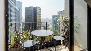 Ein Balkon mit rundem Tisch und zwei Stühlen, umgeben von Kübelpflanzen.