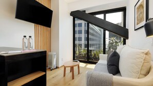 Ein modernes Wohnzimmer mit einer Couch, einem Couchtisch, einem an der Wand montierten Fernseher und einem großen Fenster mit Blick auf die Stadt.
