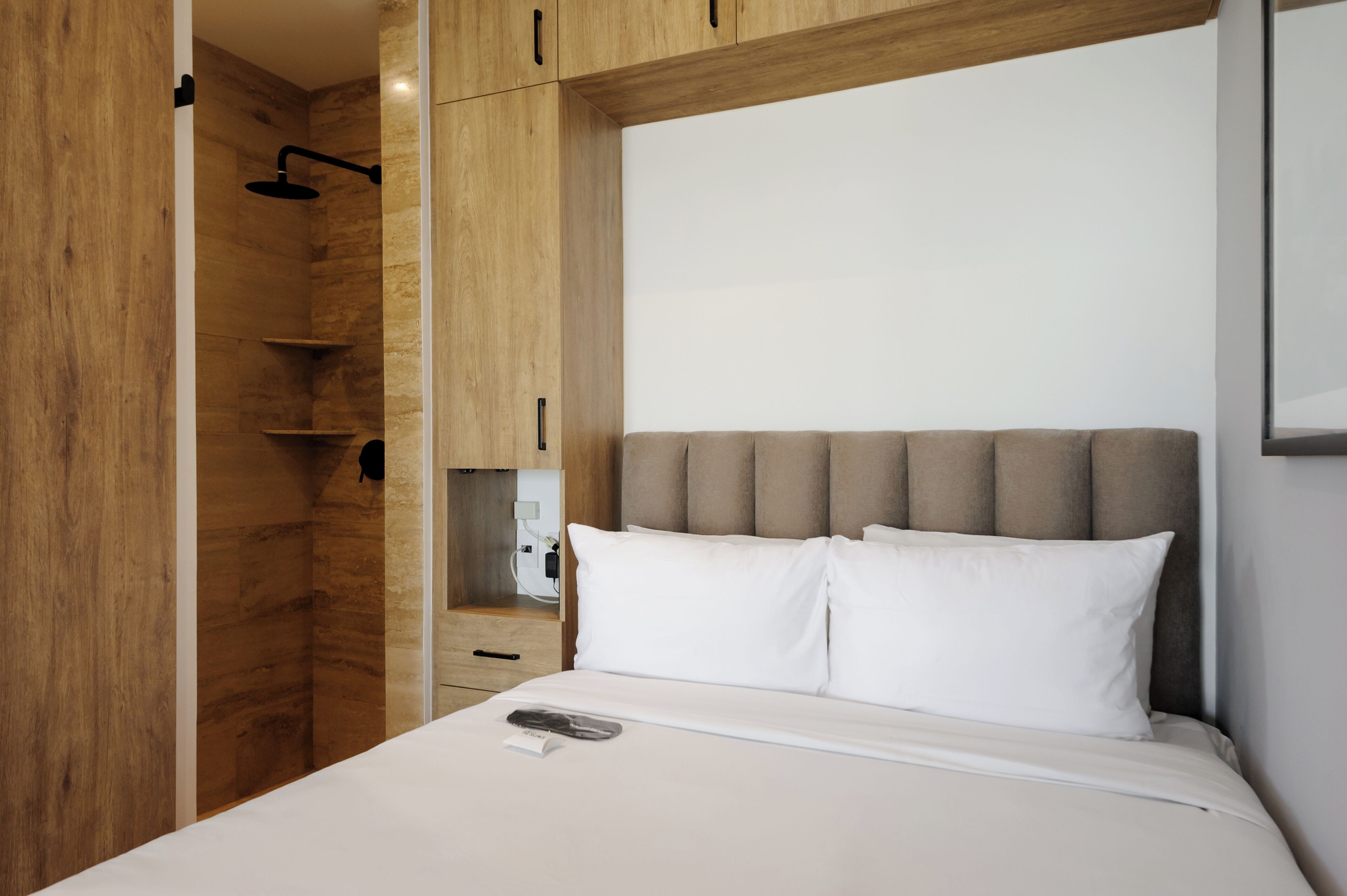 A modern hotel room with a wooden wardrobe, a bed with white linens, and a built-in shower.