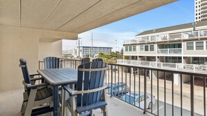 A balcony with a table and chairs, a view of a building across the street, and a clear sky. - Canvas Back 202 by Seaside Vacations & Sales (Ocean City)