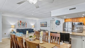 A modern kitchen with stainless steel appliances, a dining area with wooden chairs and a table, and a ceiling fan. - Canvas Back 202 by Seaside Vacations & Sales (Ocean City)