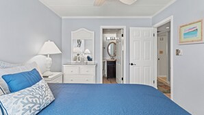 A bedroom with a bed, a nightstand, a dresser, a ceiling fan, and a door leading to another room. - Canvas Back 202 by Seaside Vacations & Sales (Ocean City)