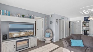 Ein Wohnzimmer mit Flachbildfernseher, grauem Sofa, einem Sessel und einem Bücherregal.