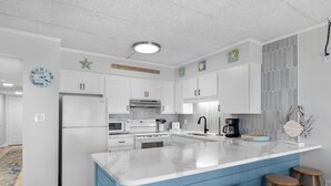 A modern kitchen with white cabinets, a central island with stools, a microwave, stove, and a coffee maker.