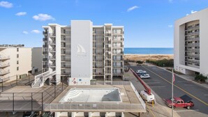 A multi-story hotel with balconies, a parking area, and a view of the beach.