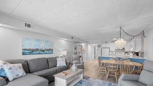 A modern living room with a grey sofa, a coffee table, and a dining area with wooden chairs and a table.