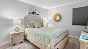 A bedroom with a bed, bedside tables, a wall-mounted mirror, and a window with blinds.