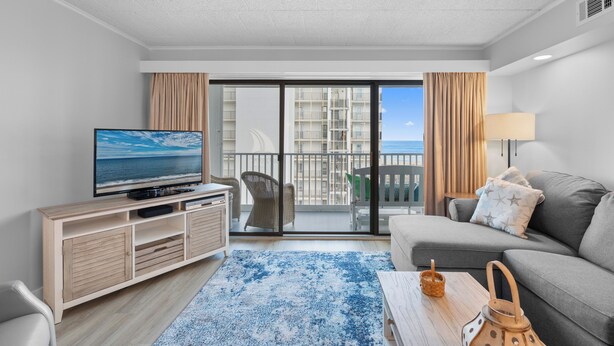 A modern living room with a television, a sofa, a coffee table, and a view of the sea through a balcony.