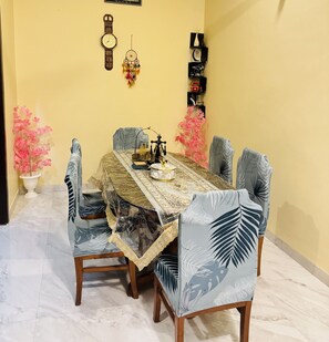Un coin repas avec une table dressée pour six personnes, entourée de chaises ornées de motifs végétaux.