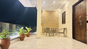 A clean, well-lit balcony with potted plants, a stone wall, and a wooden door. - Spacious 5-Bedroom Homestay with Attached Washrooms, near Amritsar Airport. (Amritsar)