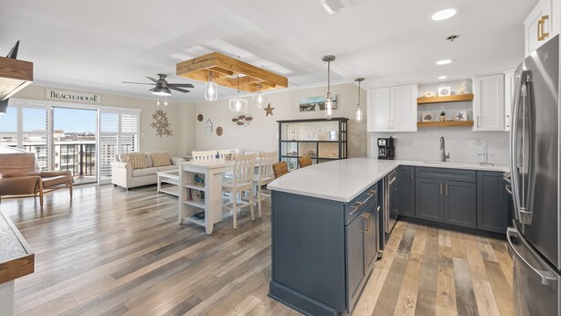 A modern kitchen with a large island, wooden flooring, and a view of the beach.
