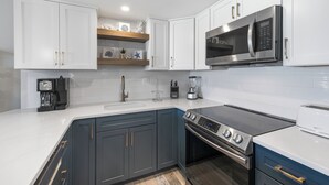 A modern kitchen with white cabinets, a stainless steel microwave, a built-in oven, and a coffee maker.