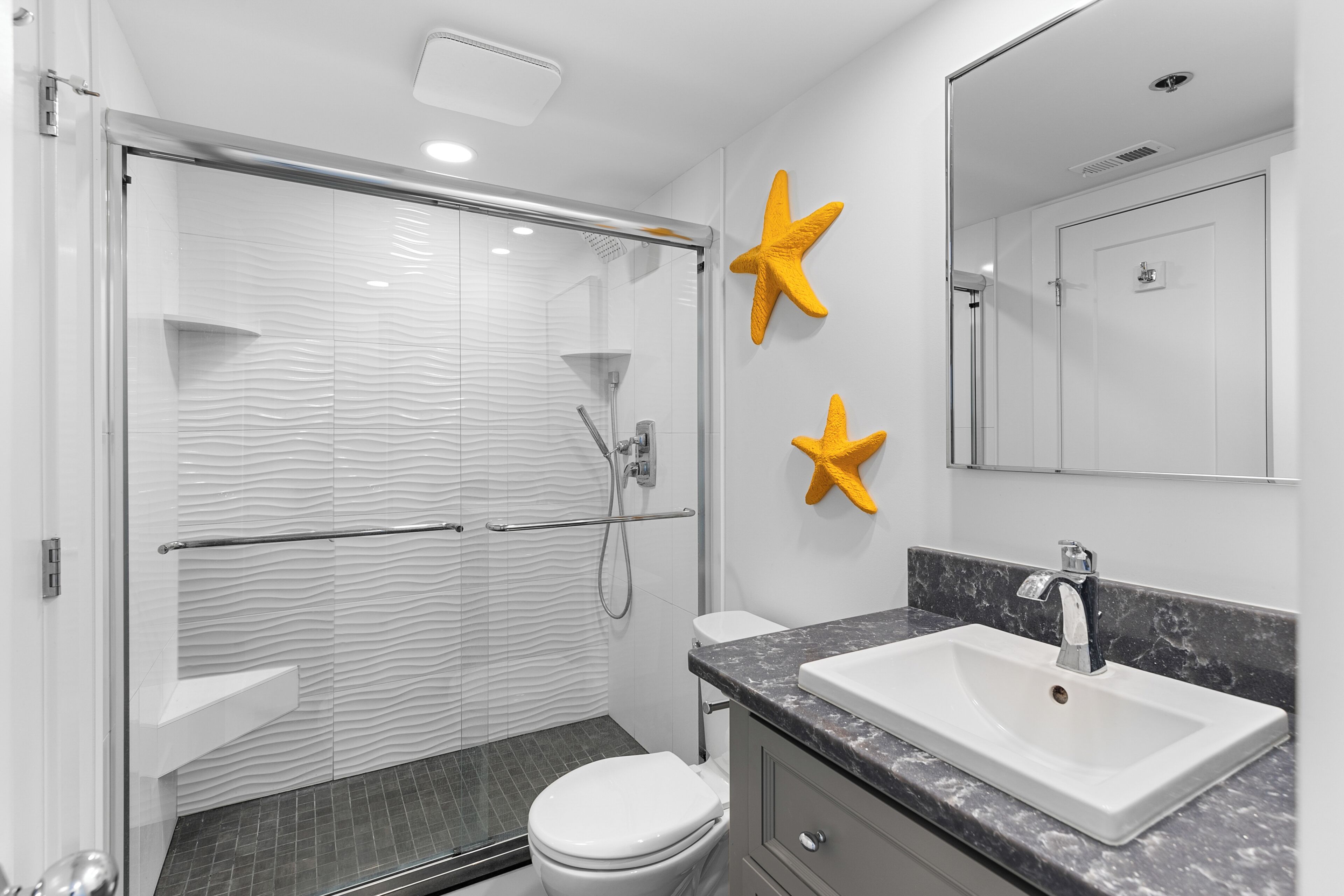 Une salle de bain moderne avec une douche à parois de verre, des toilettes blanches et un lavabo en marbre.