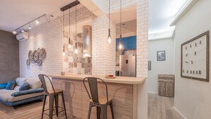 A modern kitchen with a white brick backsplash, two bar stools, a built-in island, and a hanging light fixture.