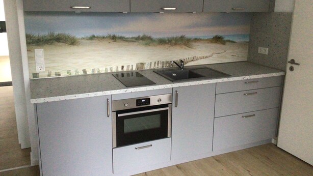 A kitchen with grey cabinets, a built-in oven, a sink, and a countertop.