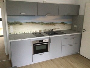 A kitchen with grey cabinets, a built-in oven, a sink, and a countertop. - Newly converted vacation apartment on the first floor  (Porta Westfalica)