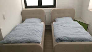 A small room with two single beds, each with a grey duvet and a pillow.