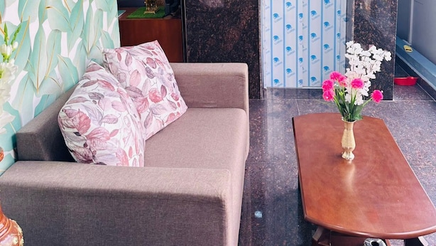 A modern living room with a sofa, a coffee table, and a decorative vase with flowers. - S G R HOTEL & LODGE (Bengaluru)