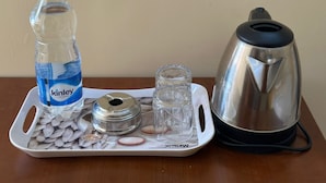 A tray with a water bottle, a glass, a metal container, and a kettle on a wooden table. - S G R HOTEL & LODGE (Bengaluru)