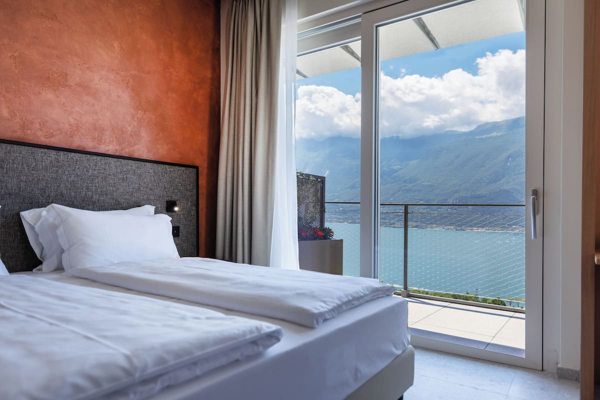 A hotel room with a large bed, a view of the sea, and a balcony with a glass door.