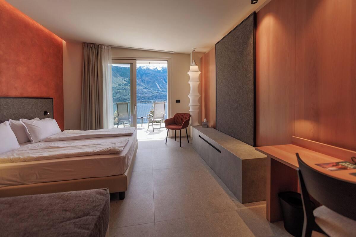 A hotel room with two beds, a desk, a chair, and a balcony with a view of mountains.