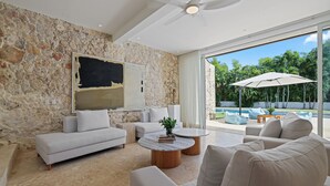 Ein modernes Wohnzimmer mit einer Steinwand, einem großen Gemälde und Blick auf einen Pool und Grünflächen.