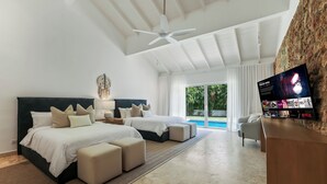 Ein modernes Schlafzimmer mit zwei Betten, einem Deckenventilator, einem Fernseher und Blick auf einen Pool.