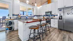 A modern kitchen with white cabinets, a stainless steel refrigerator, and a wooden island with bar stools. - Dragonfly Shores - Beach View, Pet Friendly, Beach Gear Credit Included! (St George Island)