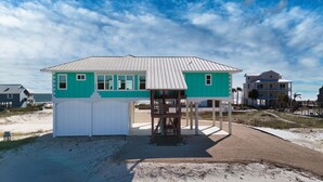 A beach house with a covered porch and a small deck, surrounded by sand and a clear sky. - Dragonfly Shores - Beach View, Pet Friendly, Beach Gear Credit Included! (St George Island)