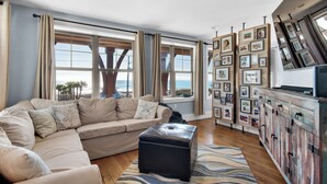 A living room with a beige sectional sofa, a black ottoman, and a wooden cabinet with framed pictures. - SNOW BIRDS ONLY.  LOOKING FOR A 3 MONTH RENTAL.  Delightful Santa Rosa Beach (Santa Rosa Beach)
