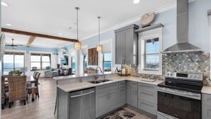 A modern kitchen with grey cabinets, stainless steel appliances, and a large island. There is a dining area with wicker chairs and a view of the ocean. - SNOW BIRDS ONLY.  LOOKING FOR A 3 MONTH RENTAL.  Delightful Santa Rosa Beach (Santa Rosa Beach)