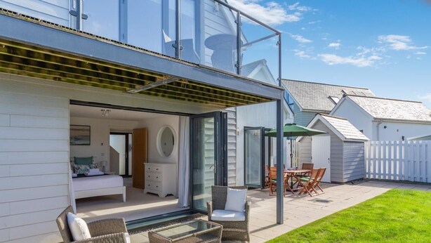 Una casa moderna con un porche acristalado, un dormitorio con cama y cómoda, y un comedor con mobiliario exterior.