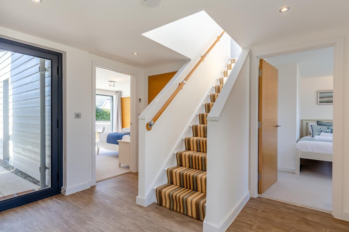 Un escalier avec des rampes en bois, une chambre à coucher avec un lit et une table de chevet, et un salon avec un canapé et une table basse.